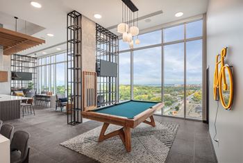 A billiard table is in the middle of a room with a view of the city.
